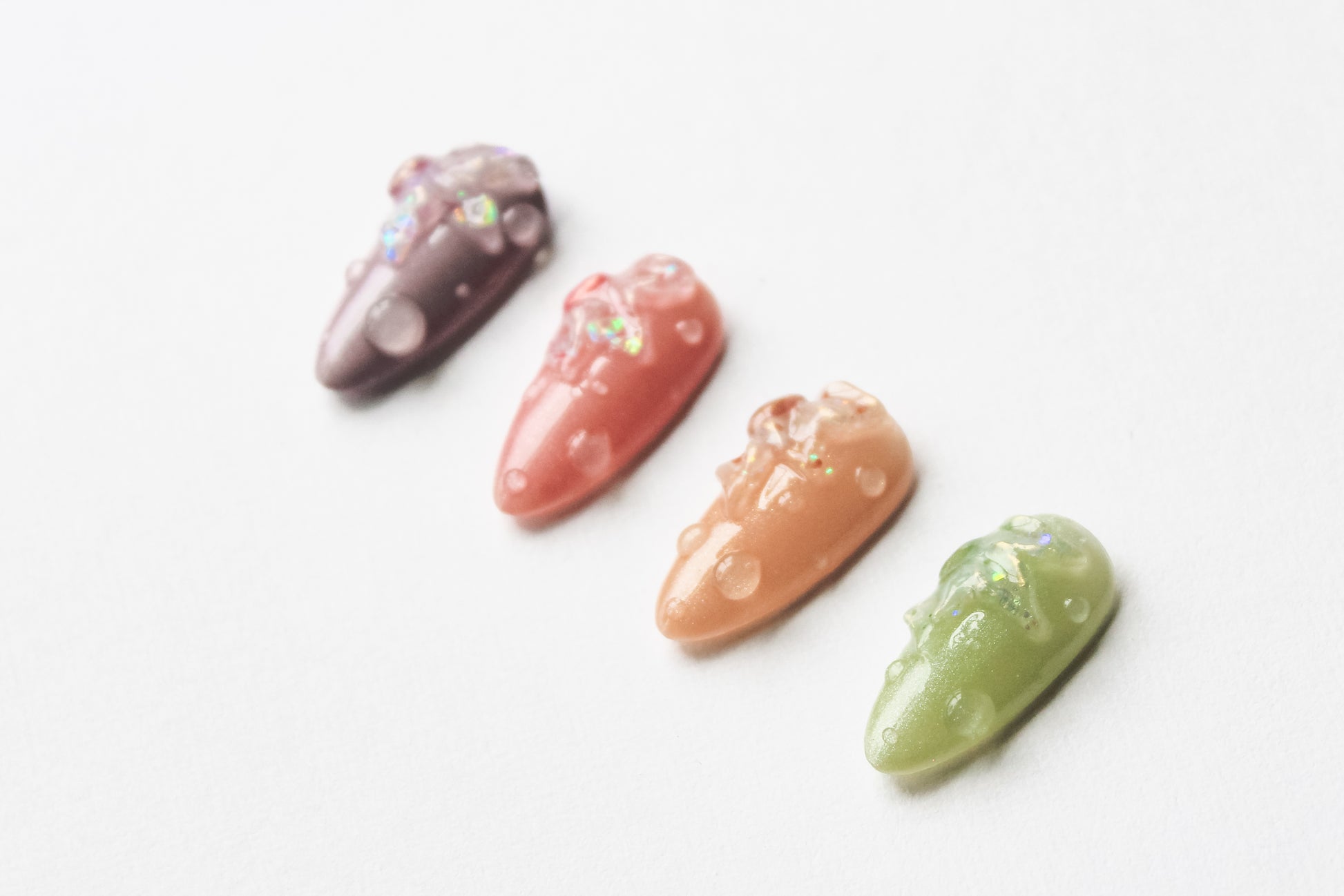A dreamy row of medium almond press-on nails in soft lilac, pink, beige, and green, each blooming with iridescent 3D florals and delicate dewdrop details.