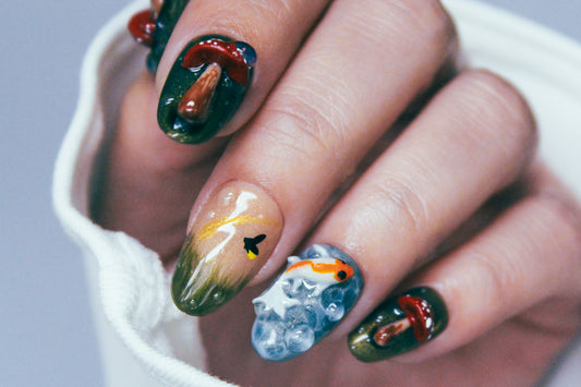 Close-up of a hand wearing 3D Enchanted Pond press-on nails, featuring sculpted mushrooms, koi fish, dewdrops, and a tiny black firefly silhouette.