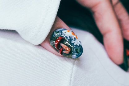 Close-up of the thumb wearing a 3D Enchanted Pond press-on nail, featuring sculpted koi fish, mushrooms, swirling water detail, and raised dewdrops.