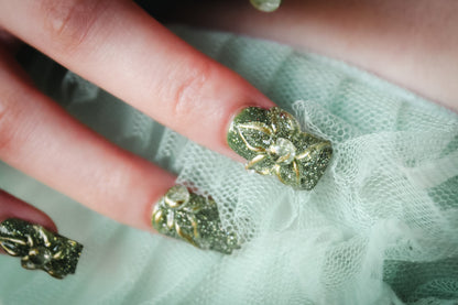 Close-up of a Green Blossom press-on nails with green glitter and clear 3D flowers outlined in gold.