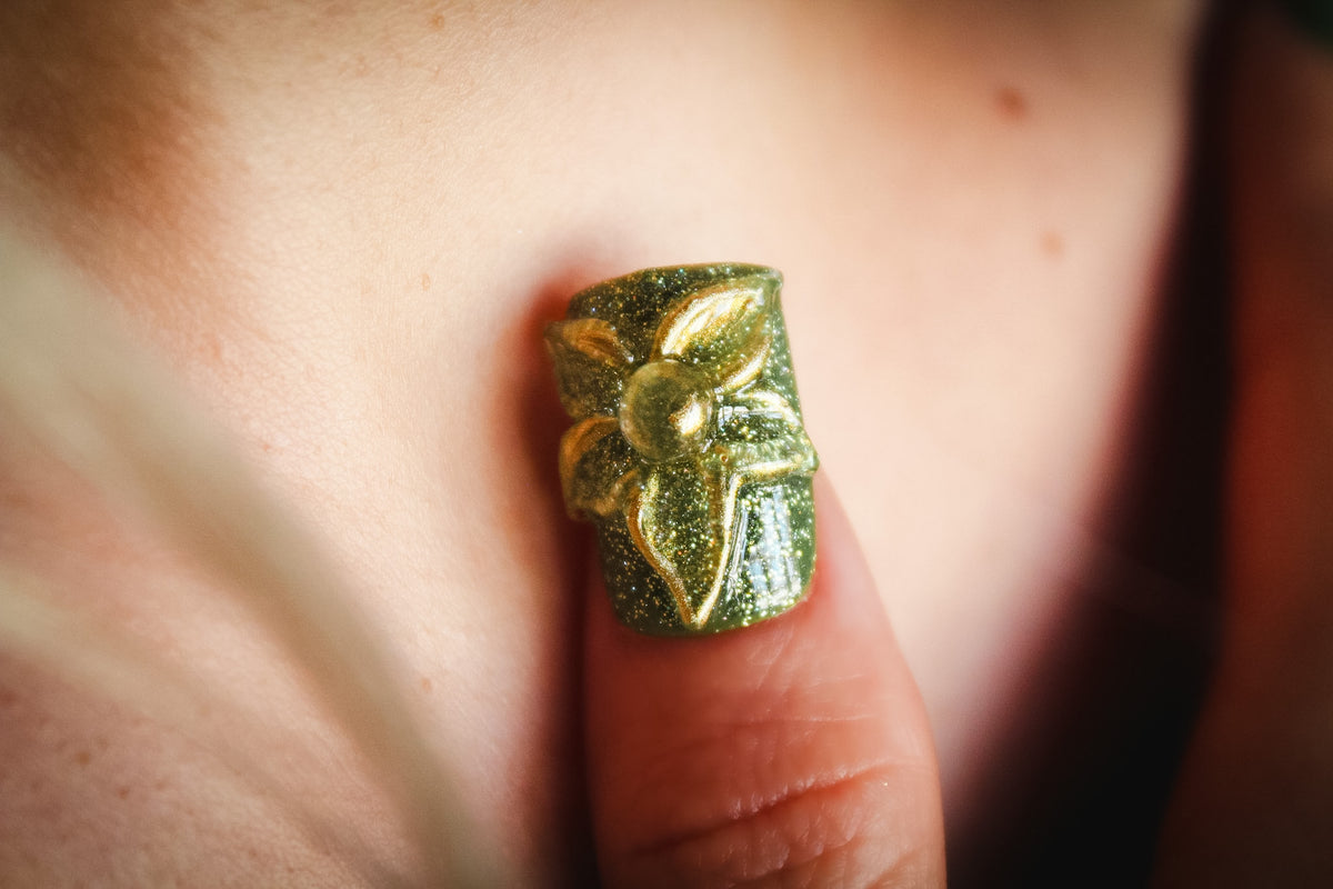 Close-up of a Green Blossom press-on nail with green glitter and a clear 3D flower outlined in gold.