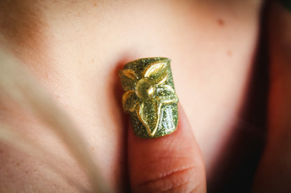 Close-up of a Green Blossom press-on nail with green glitter and a clear 3D flower outlined in gold.