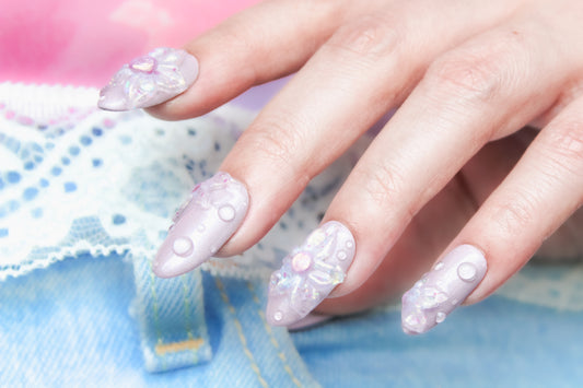 Delicate hand with medium round press-on nails in a muted lavender (Pressed Rose), adorned with shimmering 3D florals and dewdrop details, evoking a soft, ethereal garden.